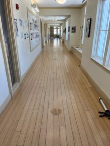 Worn bamboo plank flooring in a school hallway before refinishing showing surface wear and dark stain marks