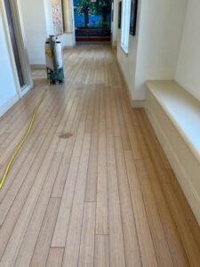School hallway bamboo floor before refinishing with sanding equipment and yellow power cord visible
