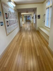 Completed bamboo floor refinishing in a school hallway with children's artwork displayed on the walls