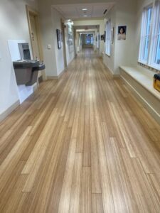 Long school hallway with refinished bamboo plank flooring showing a smooth satin finish under overhead lighting